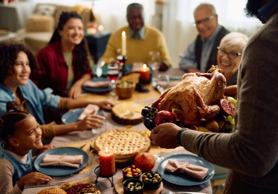 Close up of African American man serving Thanksgiving turkey to his extended family during a meal in dining room.