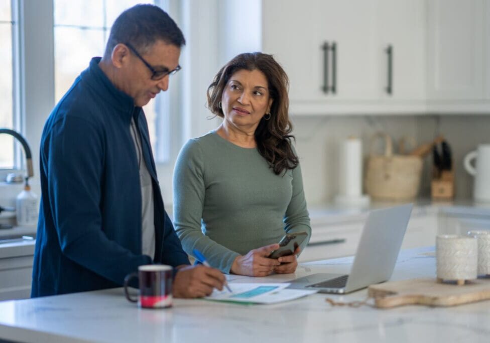 Couple working at kitchen table with laptop.